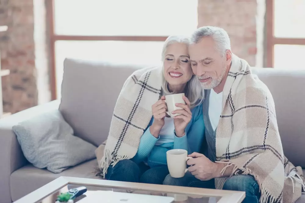 Una pareja de mayores con una manta y una taza de té sentados en el sofá
