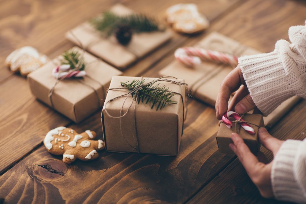 Mujer envolviendo regalos de Navidad sobre un fondo de madera con materiales sostenibles y una galleta casera.